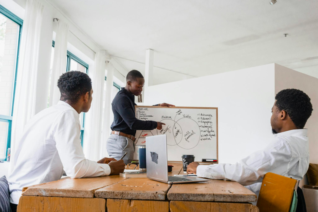 Three men engaging in a business discussion with a whiteboard presentation in a modern office setting.